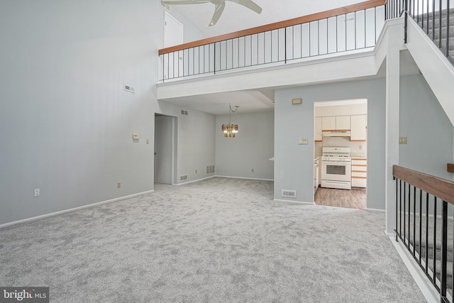 unfurnished living room with visible vents, a towering ceiling, carpet flooring, baseboards, and ceiling fan with notable chandelier