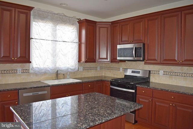 kitchen with stainless steel appliances, a sink, dark stone countertops, and tasteful backsplash