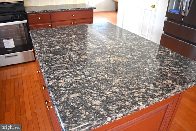 details with dark stone countertops, brown cabinetry, light wood finished floors, stainless steel range with gas stovetop, and wall oven