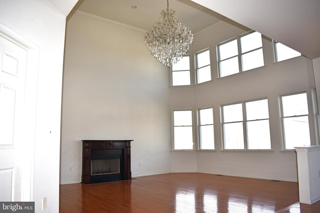 unfurnished living room with a chandelier, wood finished floors, a wealth of natural light, and a fireplace with flush hearth