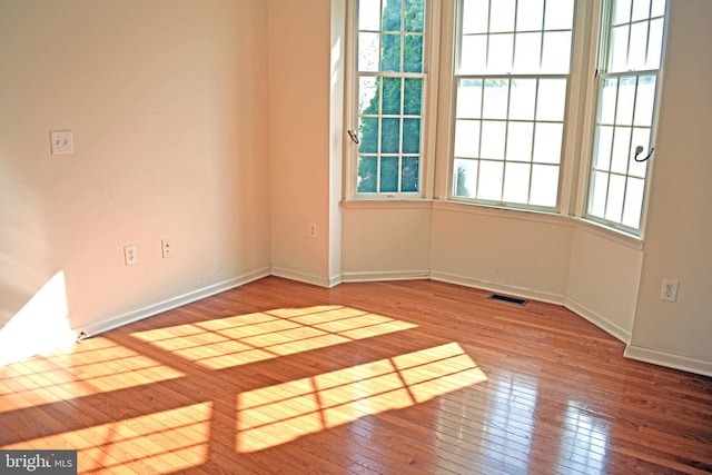 unfurnished room with baseboards, hardwood / wood-style floors, and visible vents