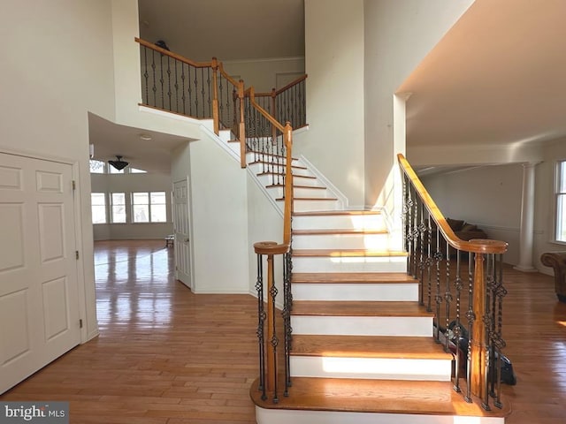 stairway featuring wood finished floors, a towering ceiling, and plenty of natural light