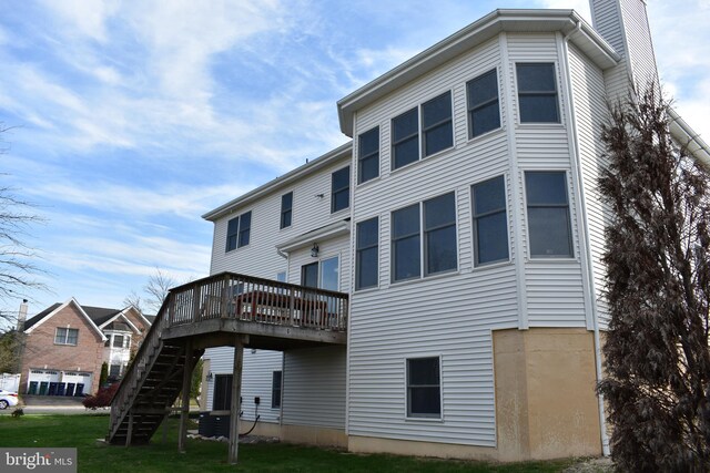 back of house with a chimney, a wooden deck, stairs, and a lawn