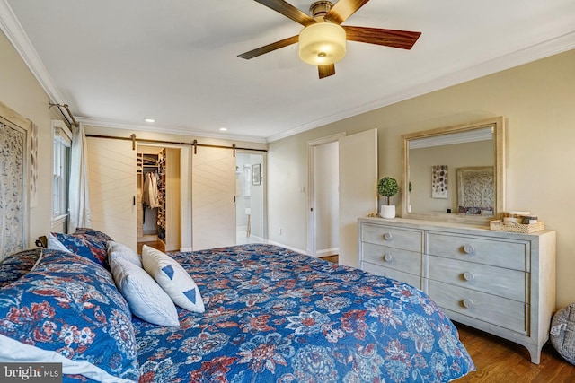 bedroom featuring a walk in closet, crown molding, a barn door, ceiling fan, and wood finished floors