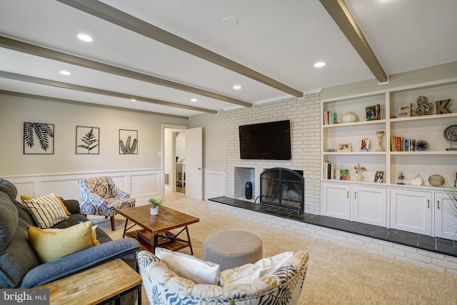 carpeted living room with built in shelves, a decorative wall, a wainscoted wall, a brick fireplace, and beamed ceiling