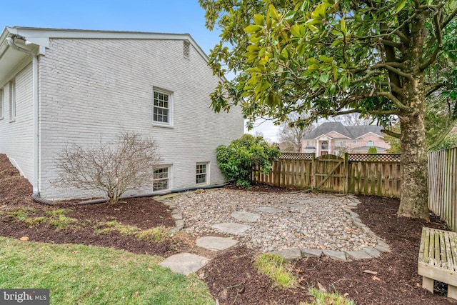 view of side of home with a gate, fence, and brick siding