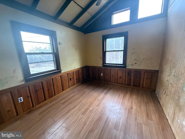 spare room with a wainscoted wall, plenty of natural light, high vaulted ceiling, and light wood-style floors