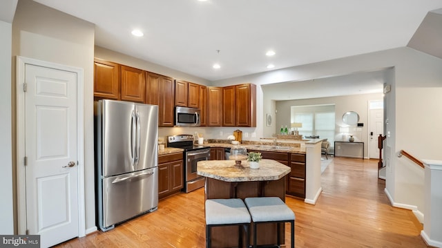 kitchen with stainless steel appliances, a peninsula, a kitchen island, light countertops, and light wood-type flooring