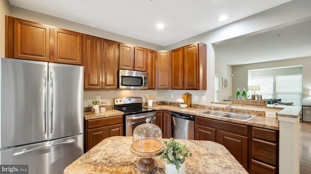 kitchen featuring a peninsula, light stone countertops, stainless steel appliances, a sink, and recessed lighting