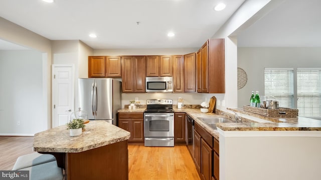 kitchen with light wood-style flooring, appliances with stainless steel finishes, a peninsula, a kitchen bar, and a sink