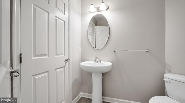 half bathroom with toilet, baseboards, and a sink