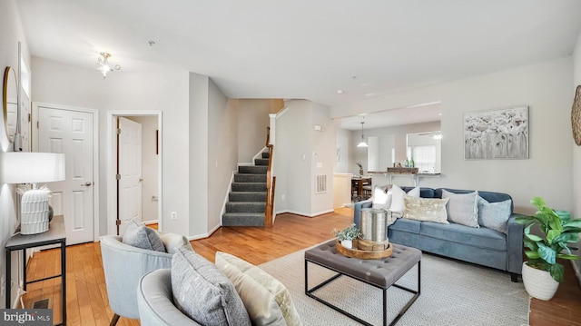 living room featuring light wood-style flooring, baseboards, and stairs