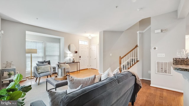 living room with light wood-type flooring, visible vents, baseboards, and stairs