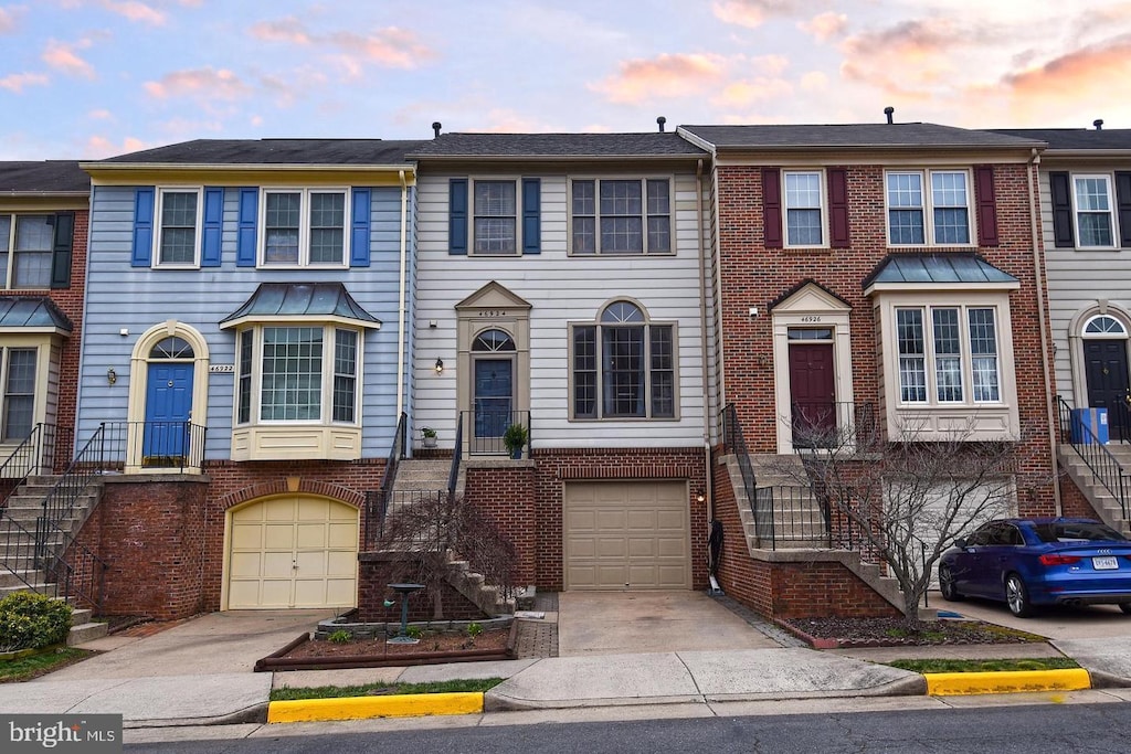 townhome / multi-family property with a garage, driveway, brick siding, and stairs