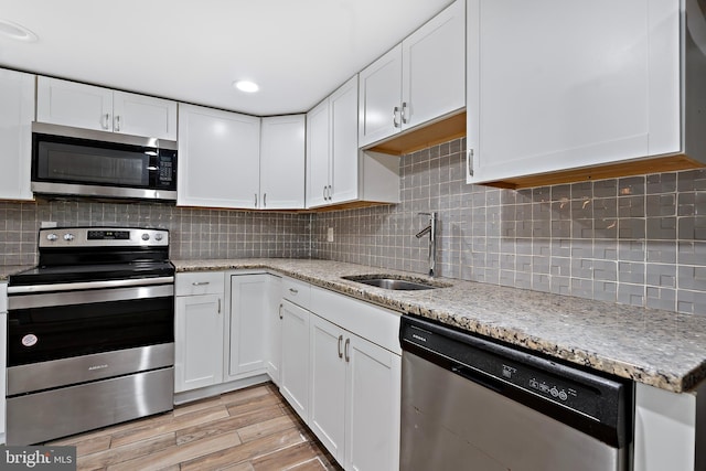 kitchen with wood finish floors, a sink, white cabinets, appliances with stainless steel finishes, and backsplash