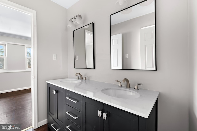 bathroom with double vanity, baseboards, a sink, and wood finished floors