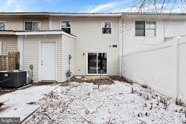 snow covered house featuring central AC unit and fence