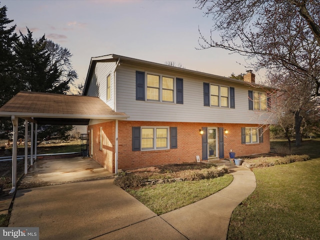 colonial inspired home featuring concrete driveway, a lawn, a chimney, a carport, and brick siding