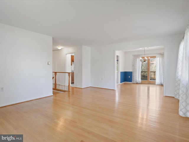 unfurnished living room with light wood-style floors, baseboards, and an inviting chandelier