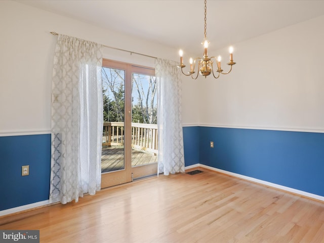 unfurnished dining area featuring a chandelier, wood finished floors, visible vents, and baseboards