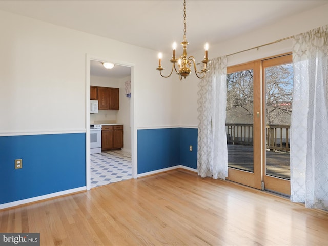 unfurnished dining area featuring light wood-type flooring, a notable chandelier, and baseboards