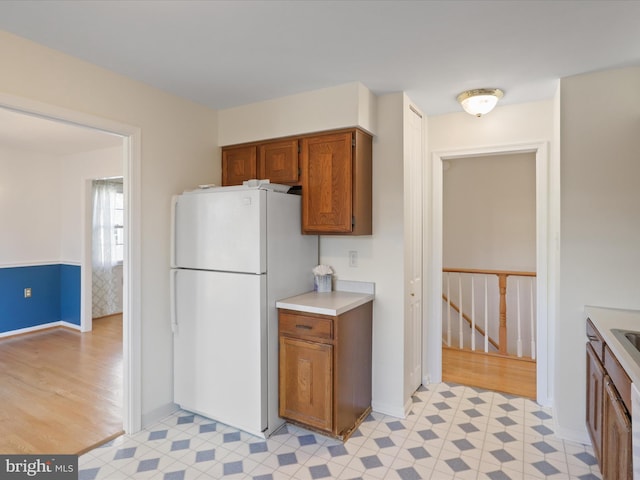 kitchen with baseboards, light countertops, freestanding refrigerator, light floors, and brown cabinetry