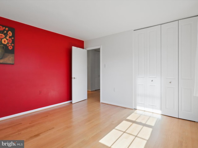 unfurnished bedroom featuring an accent wall, a closet, baseboards, and wood finished floors