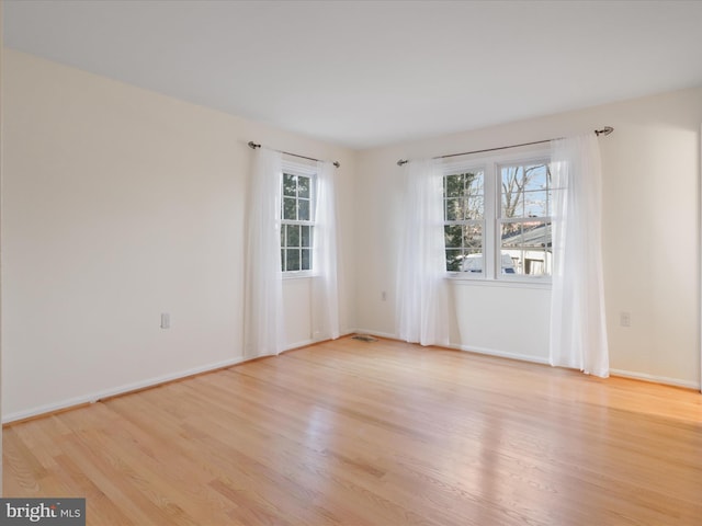 unfurnished room featuring light wood finished floors, visible vents, and baseboards