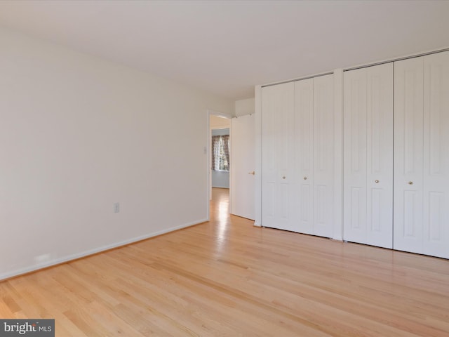 unfurnished bedroom featuring baseboards, two closets, and light wood-style floors