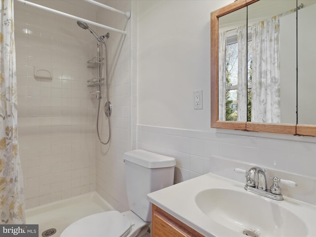 bathroom featuring a wainscoted wall, tile walls, toilet, vanity, and tiled shower