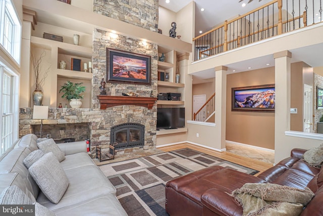 living room with stairs, a stone fireplace, built in shelves, and baseboards