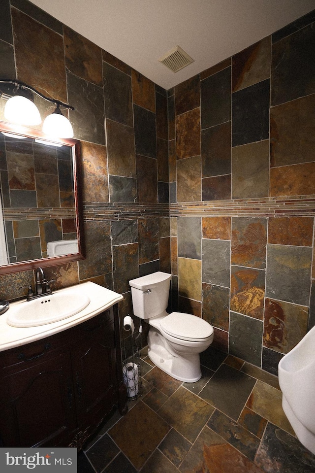 bathroom featuring tile walls, visible vents, vanity, and toilet