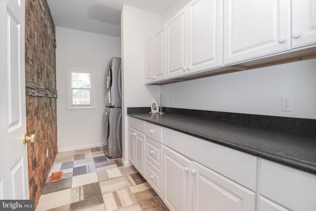 laundry area featuring cabinet space, baseboards, stacked washer and dryer, and light floors