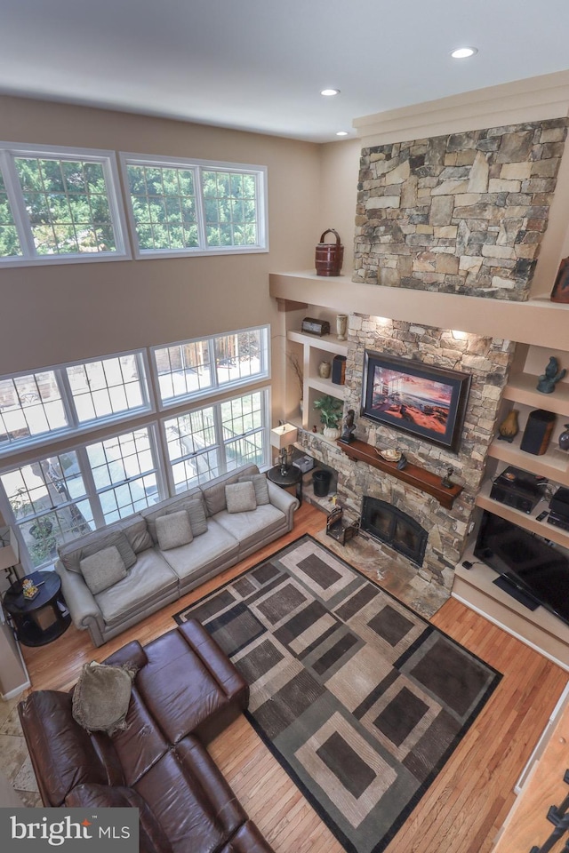 living room with recessed lighting, a fireplace, a towering ceiling, and wood finished floors