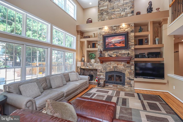 living area with a stone fireplace, wood finished floors, a high ceiling, and built in features