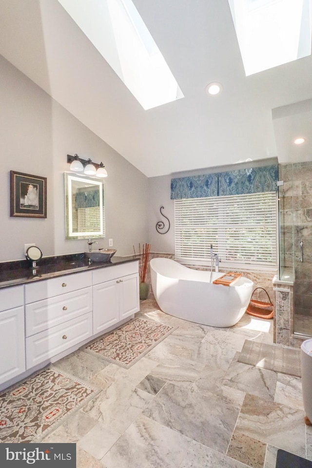 full bath featuring vaulted ceiling with skylight, marble finish floor, vanity, a freestanding tub, and a shower stall