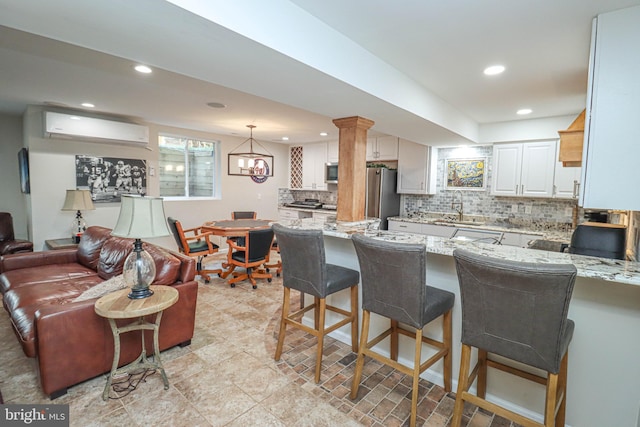 kitchen featuring light stone counters, a wall unit AC, backsplash, a sink, and a peninsula