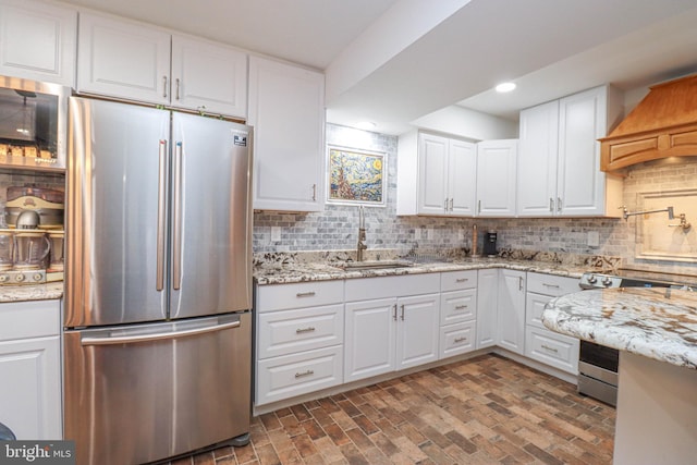 kitchen with stainless steel appliances, backsplash, white cabinetry, a sink, and light stone countertops