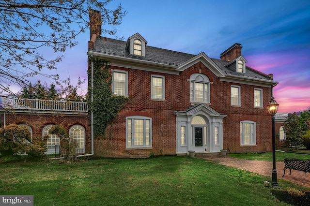georgian-style home with a lawn, brick siding, a chimney, and a high end roof