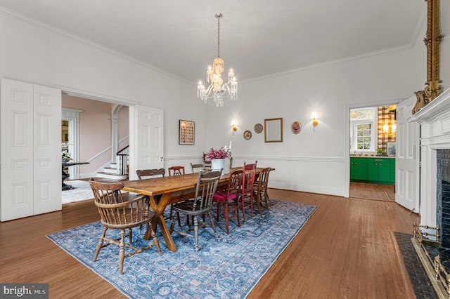 dining space featuring crown molding, a brick fireplace, an inviting chandelier, and wood finished floors