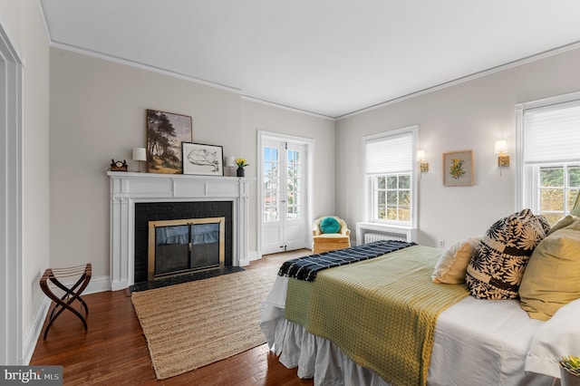 bedroom featuring a fireplace with flush hearth, dark wood-type flooring, baseboards, and crown molding