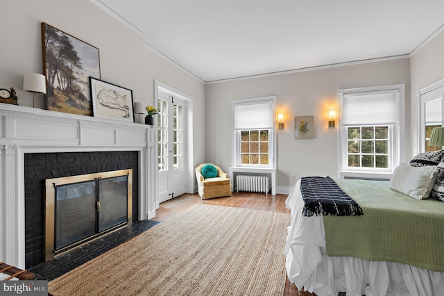 bedroom with a fireplace with flush hearth, radiator, wood finished floors, and ornamental molding