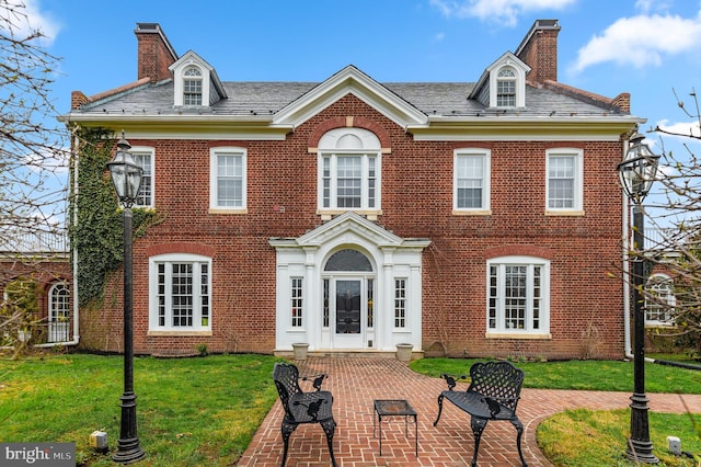 view of front facade featuring a chimney, a front yard, and brick siding