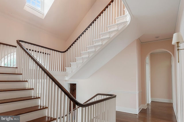 stairs with a healthy amount of sunlight, arched walkways, baseboards, and wood finished floors