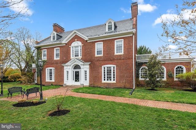 colonial inspired home featuring a front yard, a high end roof, brick siding, and a chimney
