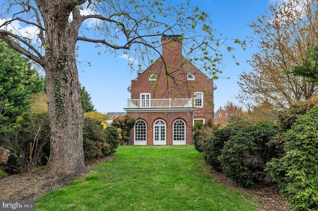 rear view of property with a yard, a chimney, brick siding, a balcony, and french doors