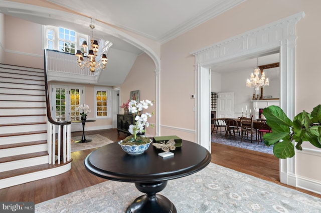foyer featuring an inviting chandelier, wood-type flooring, ornamental molding, and stairs