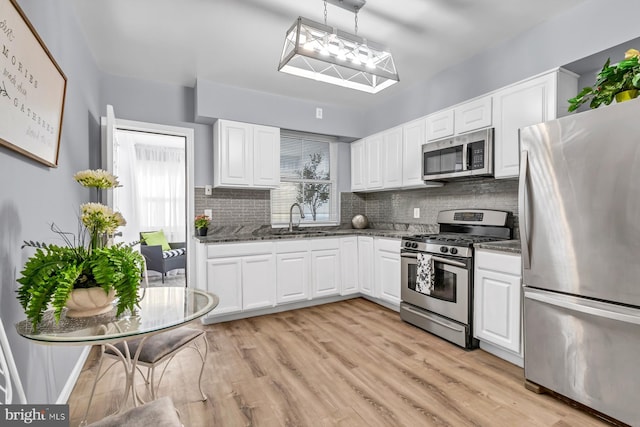 kitchen with stainless steel appliances, backsplash, light wood-style flooring, white cabinets, and a sink