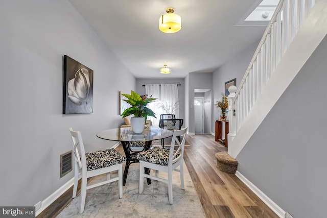 dining area with wood finished floors, visible vents, baseboards, and stairs