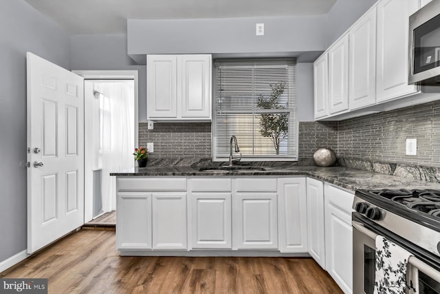 kitchen featuring dark wood-style flooring, stainless steel appliances, white cabinets, a sink, and dark stone countertops